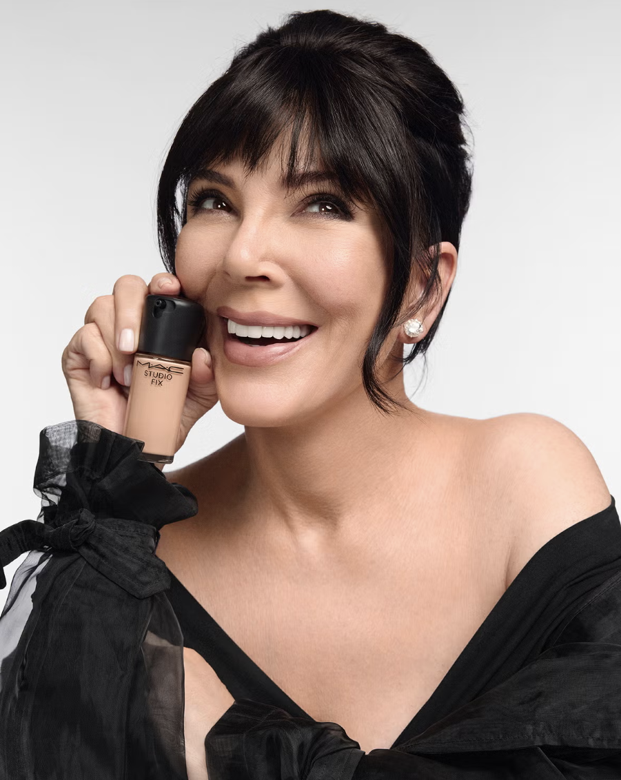 Kris Jenner smiling while holding a bottle of M·A·C Studio Fix Fluid foundation.