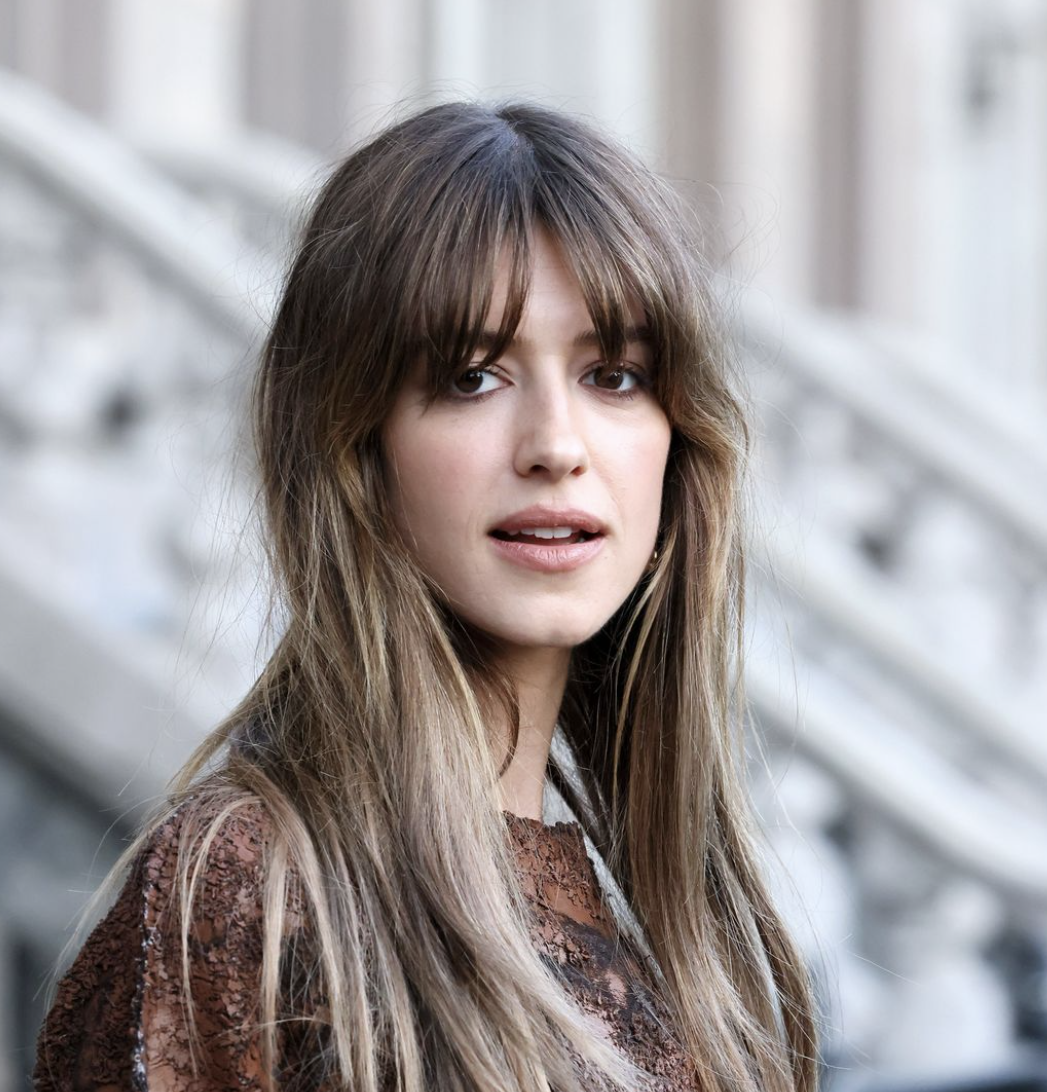 Portrait of a woman with long brunette hair featuring a textured curtain fringe and soft blonde highlights.